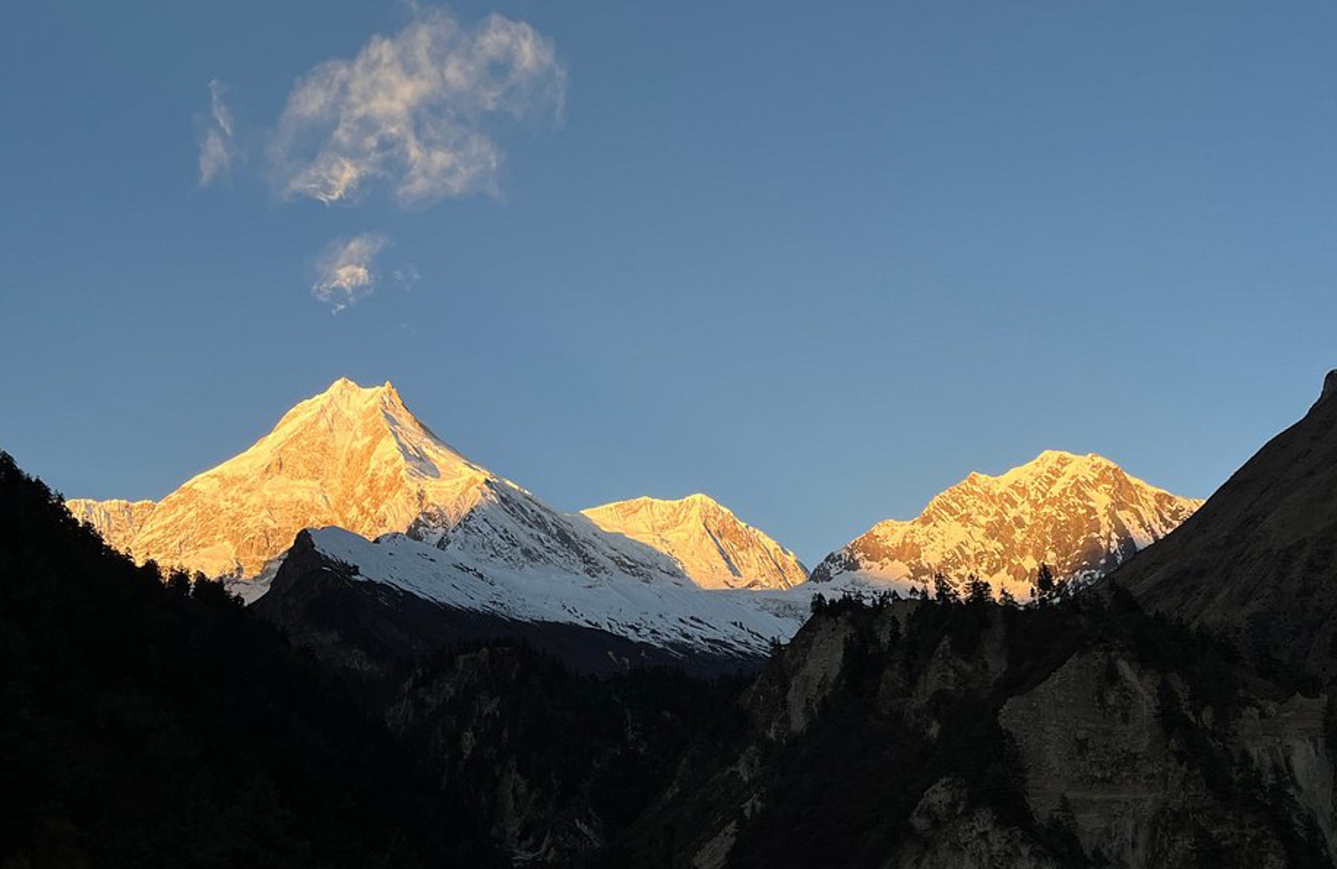Sunset view of Manaslu from Manaslu basecamp, golden light on snow-capped peaks and rugged terrain.