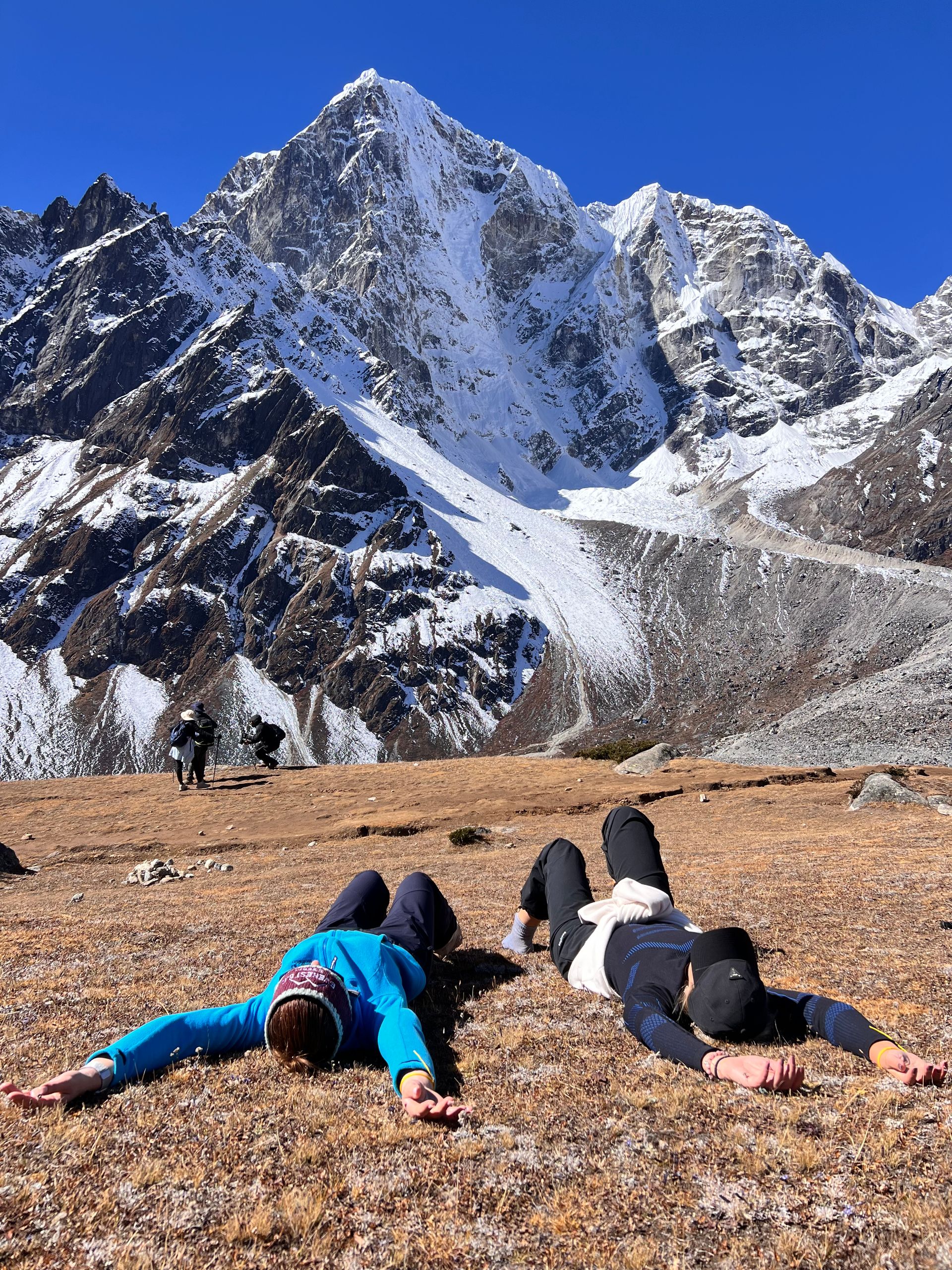 Two trekkers lying on the ground, gazing at the Himalayan mountain view during an Everest Base Camp trek.