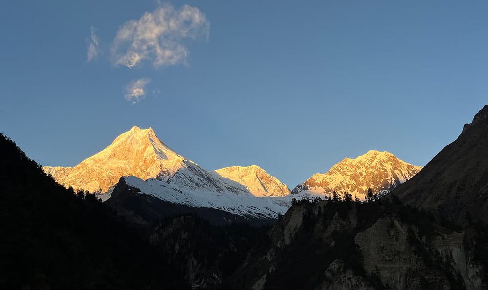 Sunset view of Manaslu from Manaslu basecamp, golden light on snow-capped peaks and rugged terrain.