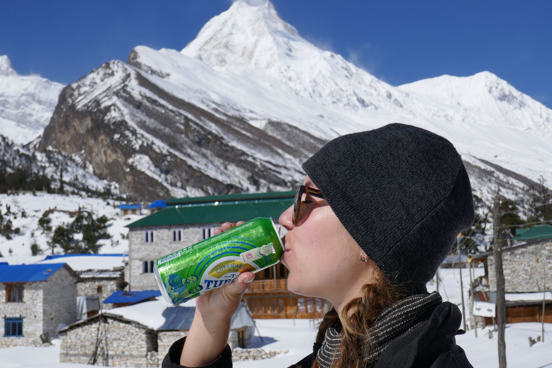 Elan, a client, smiles while holding a beer can with the snow-capped Manaslu peak rising behind her.