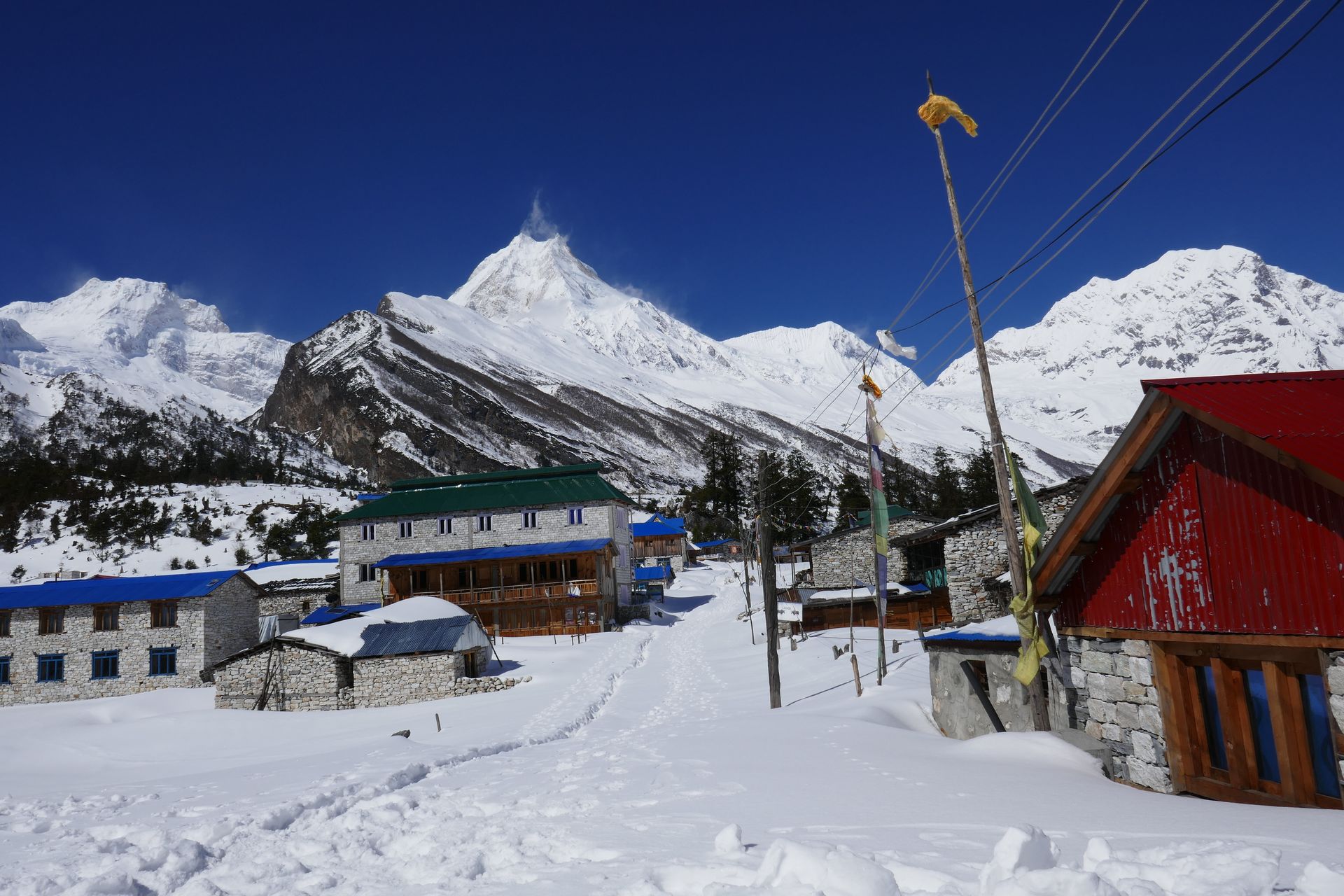 A view of Mount Manaslu rising above Shyala village, with traditional stone houses and terraced fields in the foreground.